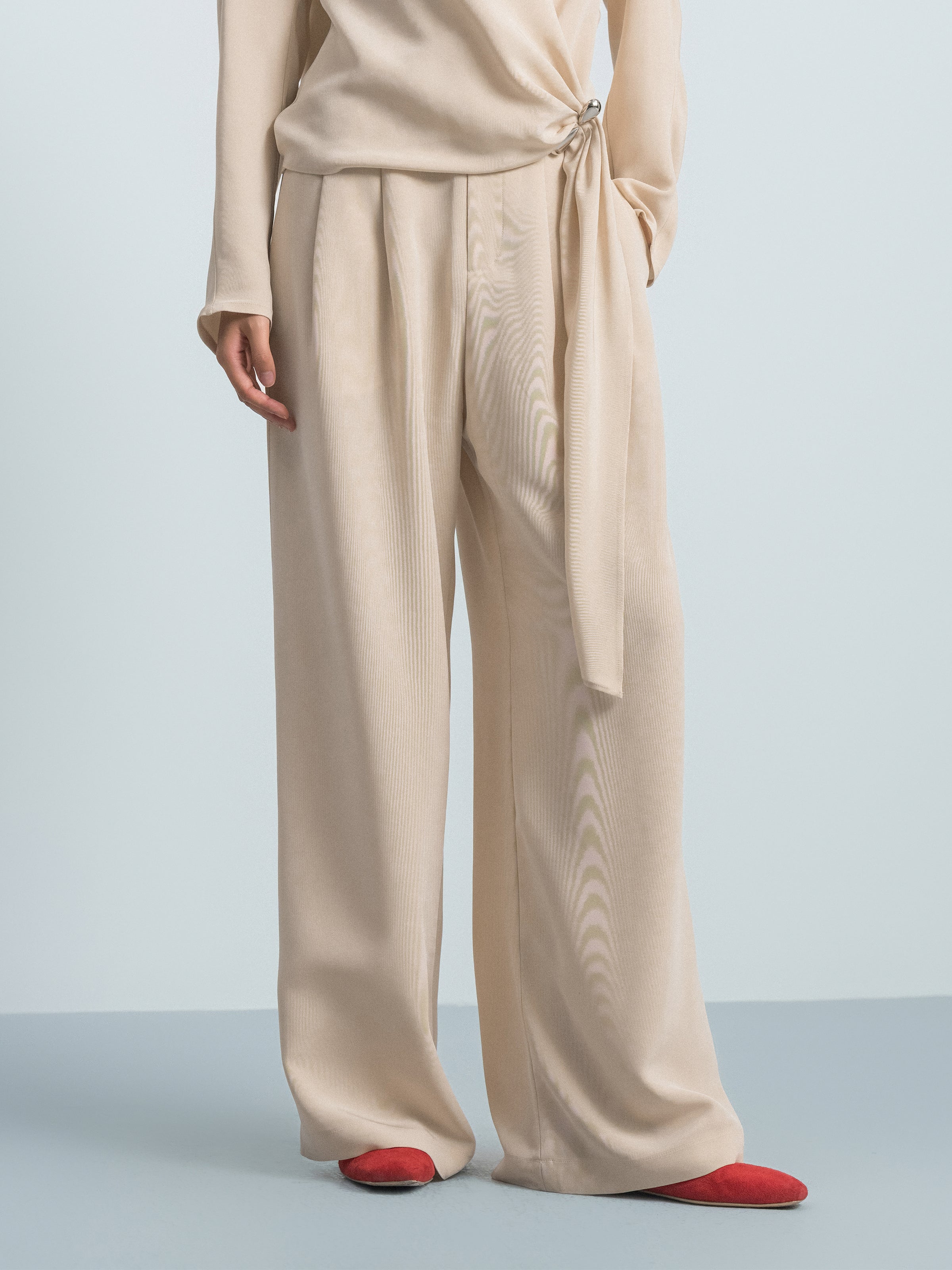 Beige satin wide-leg trousers with tie waist detail and wide pant legs.
