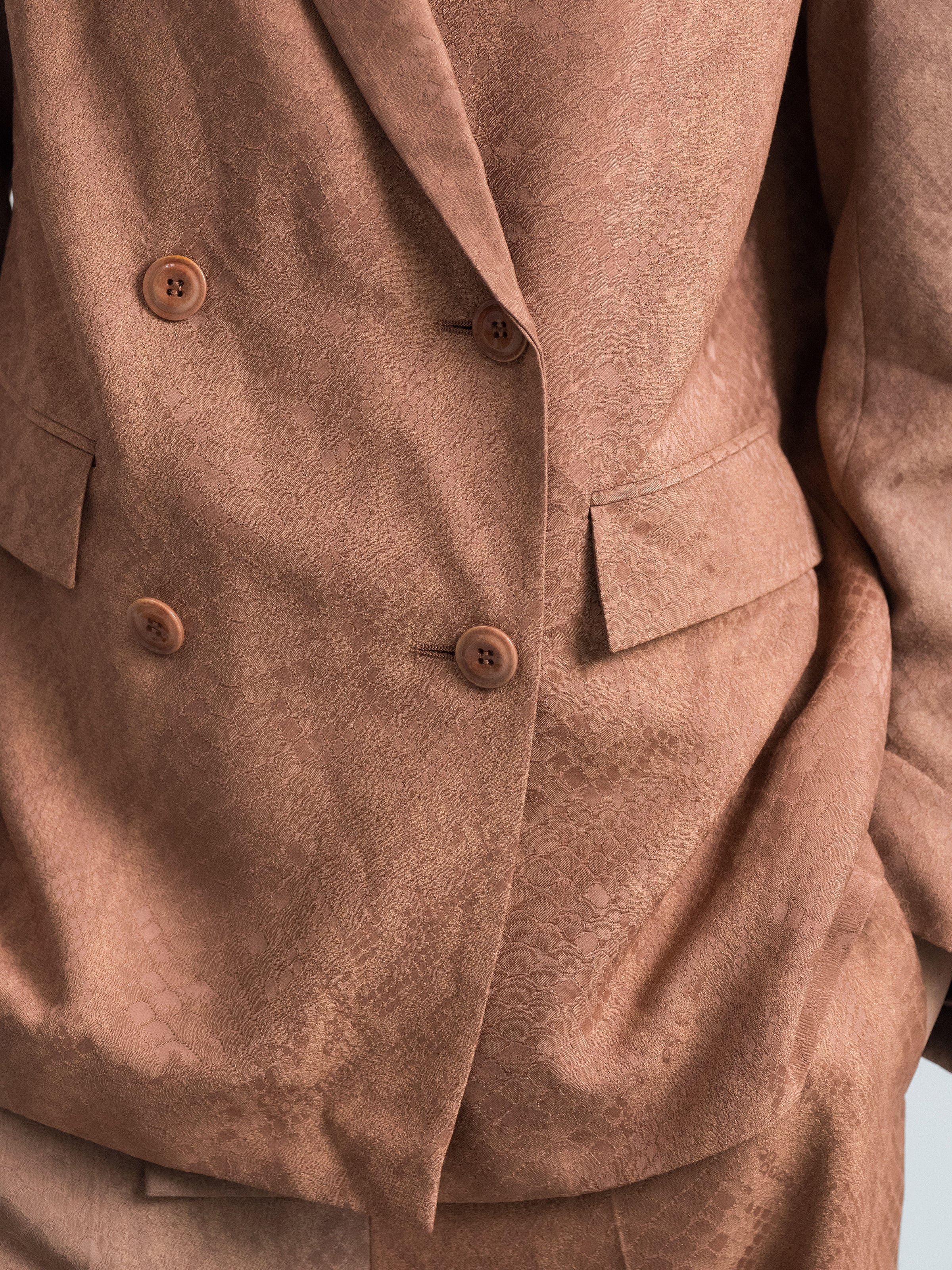 Nude blazer fabric close-up with two-button front and flap pocket