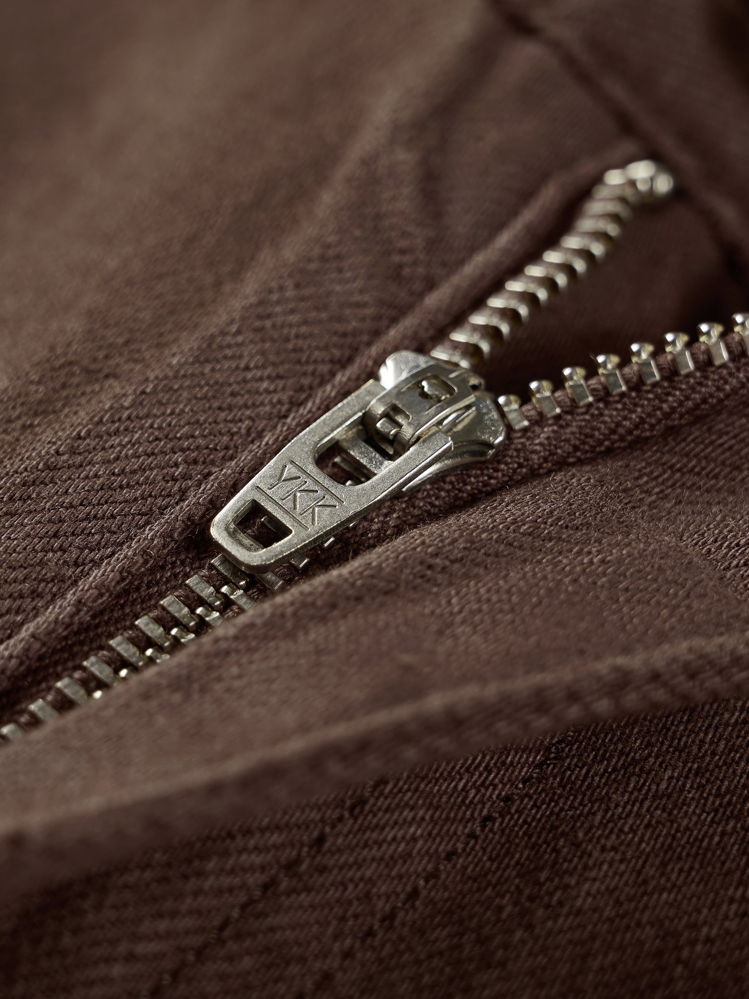 Coffee-brown jeans zipper close-up with metal pull and teeth