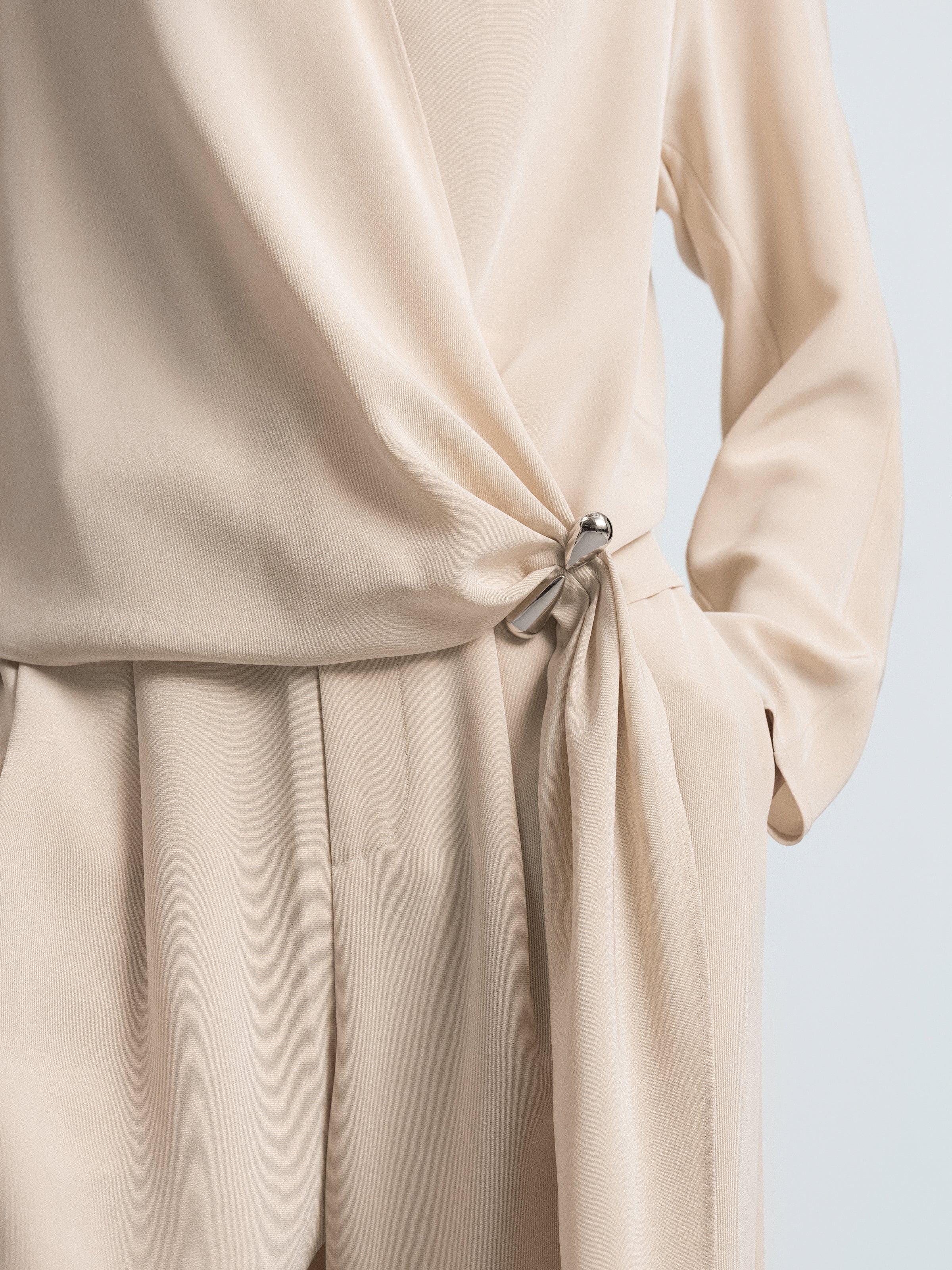 Close-up of light beige gathered waist tie on cross-over top with pleated hem